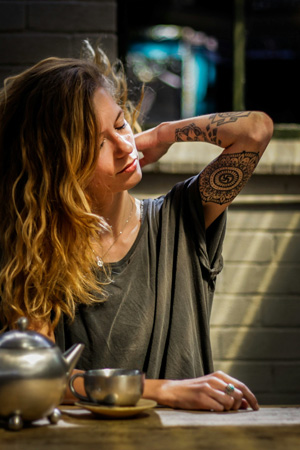 A woman appears to stretch her neck while sitting relaxed at a table with a cup of tea, a common aftercare scene following a lymphatic massage