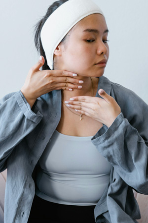 A woman demonstrating self lymphatic drainage massage techniques on her neck to promote wellness.