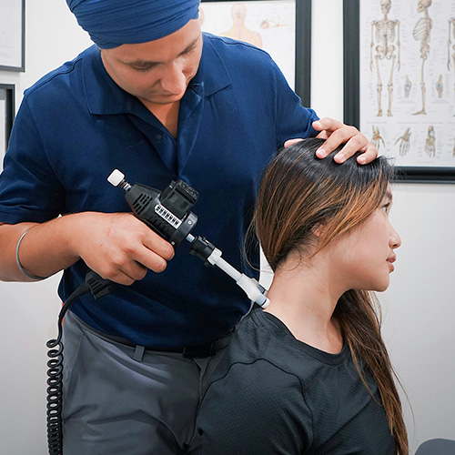 A chiropractor uses a percussive therapy device on a patient's neck to alleviate tension and improve mobility
